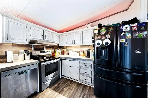 a kitchen with stainless steel appliances granite countertop a stove top oven a sink dishwasher and white cabinets with wooden floor