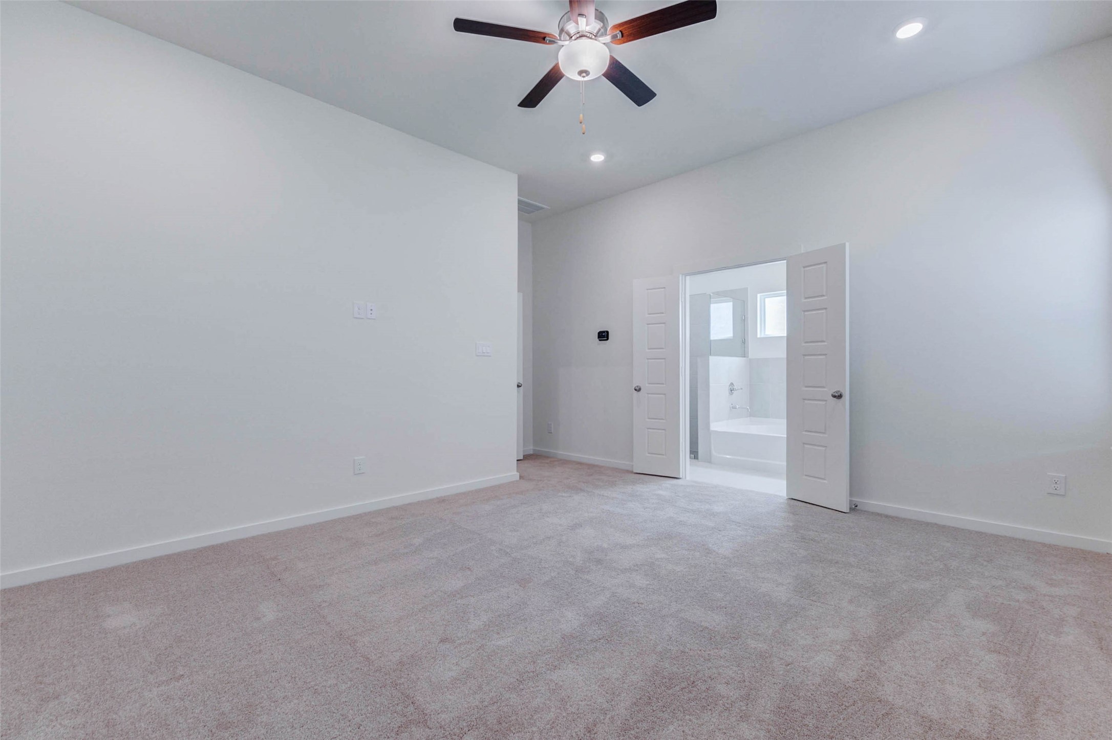6467 Escondido Drive Rosharon, TX 77583 - Photo 17 of 32 Primary bedroom view showcasing the private en-suite bath entry, plush carpet, high ceiling, ceiling fan, and recessed lighting. The room feels open and serene, with a flexible wall layout for furniture placement and direct access to the bathroom for added everyday convenience.