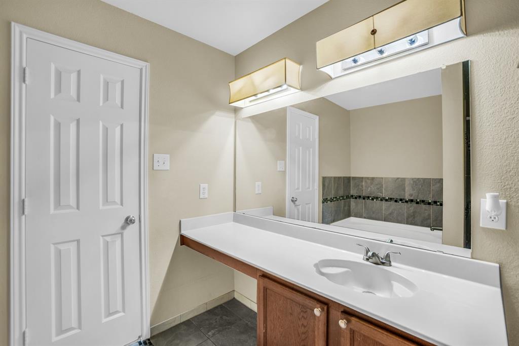 5718 Green Ivy Road Denton, TX 76210 - Photo 19 of 37 Bathroom vanity featuring a white countertop with integrated sink, wood-finish cabinetry, and a large wall-mounted mirror