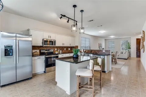 a kitchen with stainless steel appliances kitchen island granite countertop a table chairs refrigerator and a stove