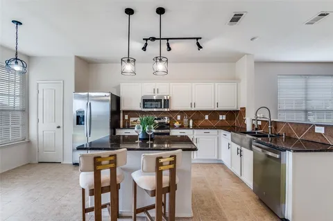 a kitchen with stainless steel appliances a sink a stove a refrigerator cabinets and a dining table