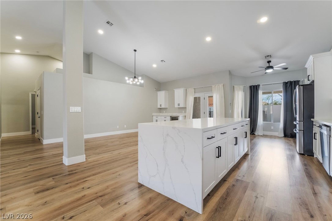 9171 West Viking Road Las Vegas, NV 89147 - Photo 18 of 43 A sleek island kitchen featuring white cabinetry and warm wood flooring seamlessly integrates with the living area.