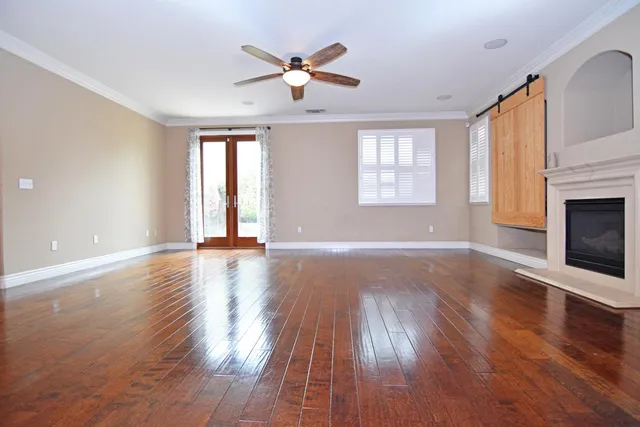 an empty room with wooden floor chandelier fan and windows