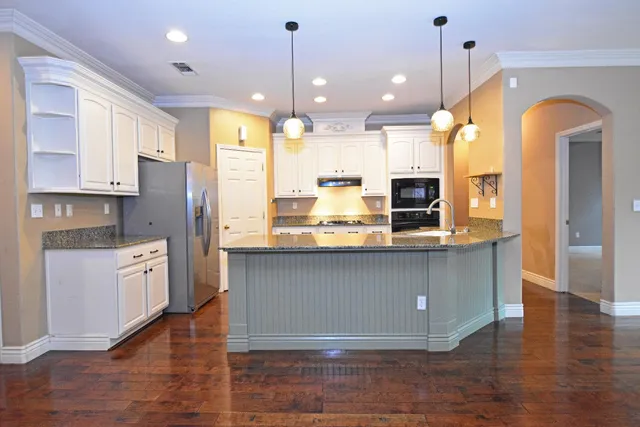 a kitchen with stainless steel appliances granite countertop a refrigerator a sink dishwasher a oven and a dining table with wooden floor