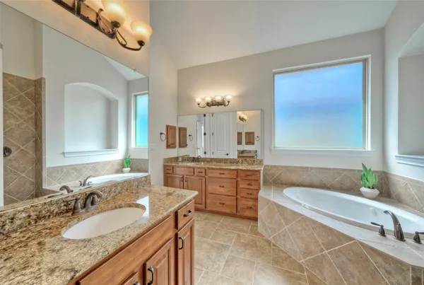a bathroom with a granite countertop double vanity sink a mirror and a bathtub
