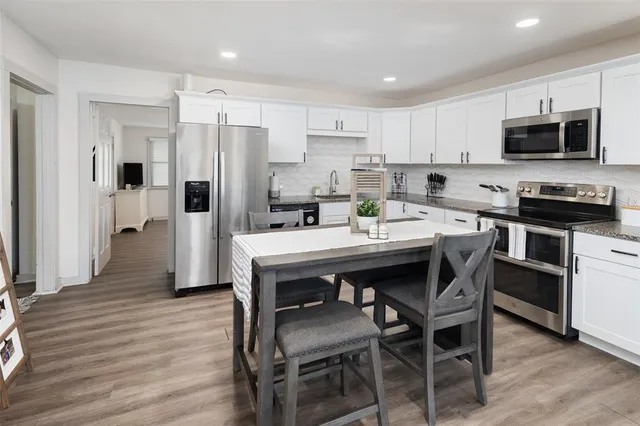 a kitchen with stainless steel appliances a dining table chairs microwave and refrigerator