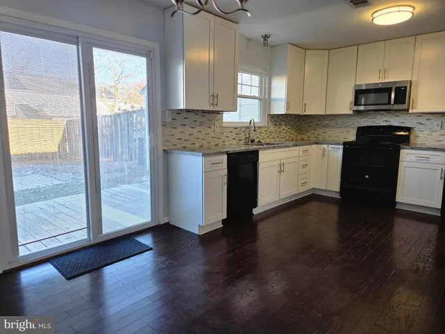 a kitchen with granite countertop wooden floors white cabinets and stainless steel appliances