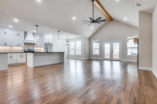 a view of an empty room and kitchen with wooden floor