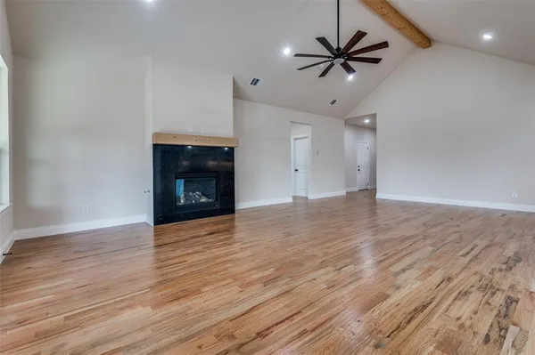 an empty room with wooden floor a ceiling fan a fireplace and windows