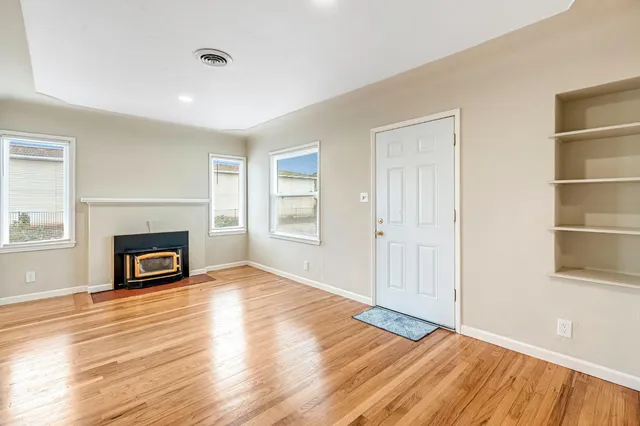 an empty room with wooden floor fireplace and windows