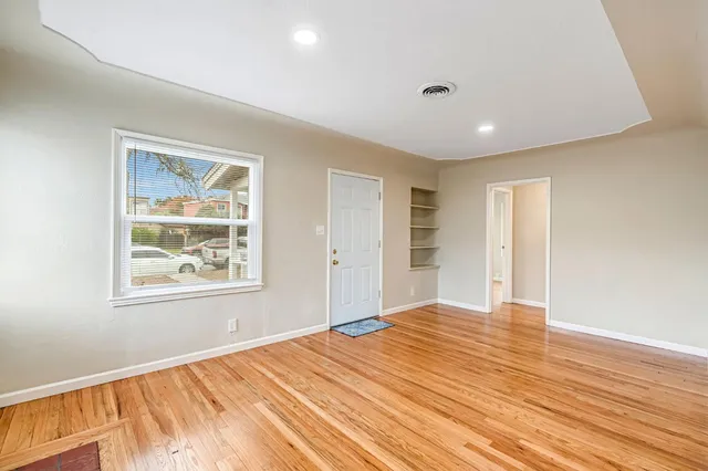 a view of an empty room with wooden floor and a window
