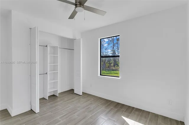an empty room with wooden floor ceiling fan and windows