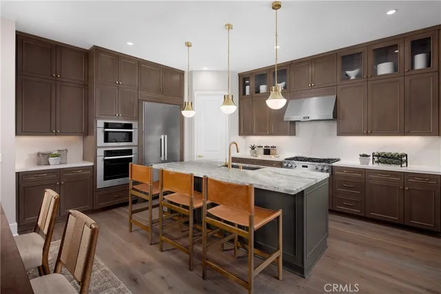 a kitchen with stainless steel appliances granite countertop a stove a sink dishwasher a refrigerator and a dining table with wooden floor