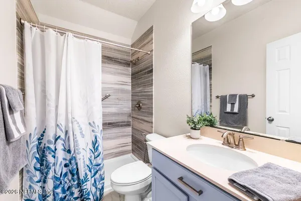 a bathroom with a granite countertop sink a toilet a mirror and shower curtain