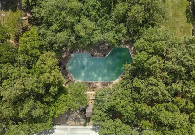 an aerial view of a residential houses with outdoor space and trees all around