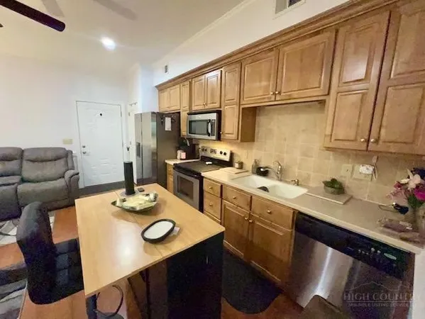a kitchen with stainless steel appliances granite countertop a sink a stove a refrigerator a dining table and chairs with wooden floor