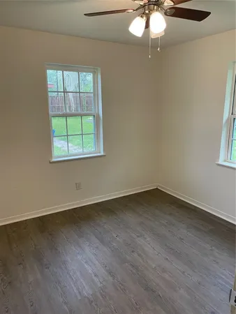 an empty room with wooden floor fan and windows