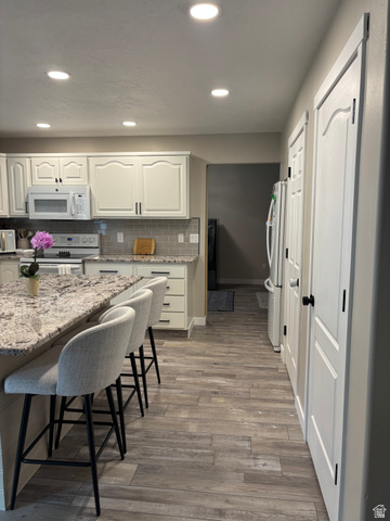 1324 West Raintree Drive, Unit 44 Price, UT 84501 - Photo 4 of 25 Kitchen featuring wood-finish tile flooring, recessed lighting, white cabinetry with dark hardware, a stone countertop, and a tiled backsplash