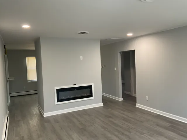a view of an empty room with wooden floor and a fireplace