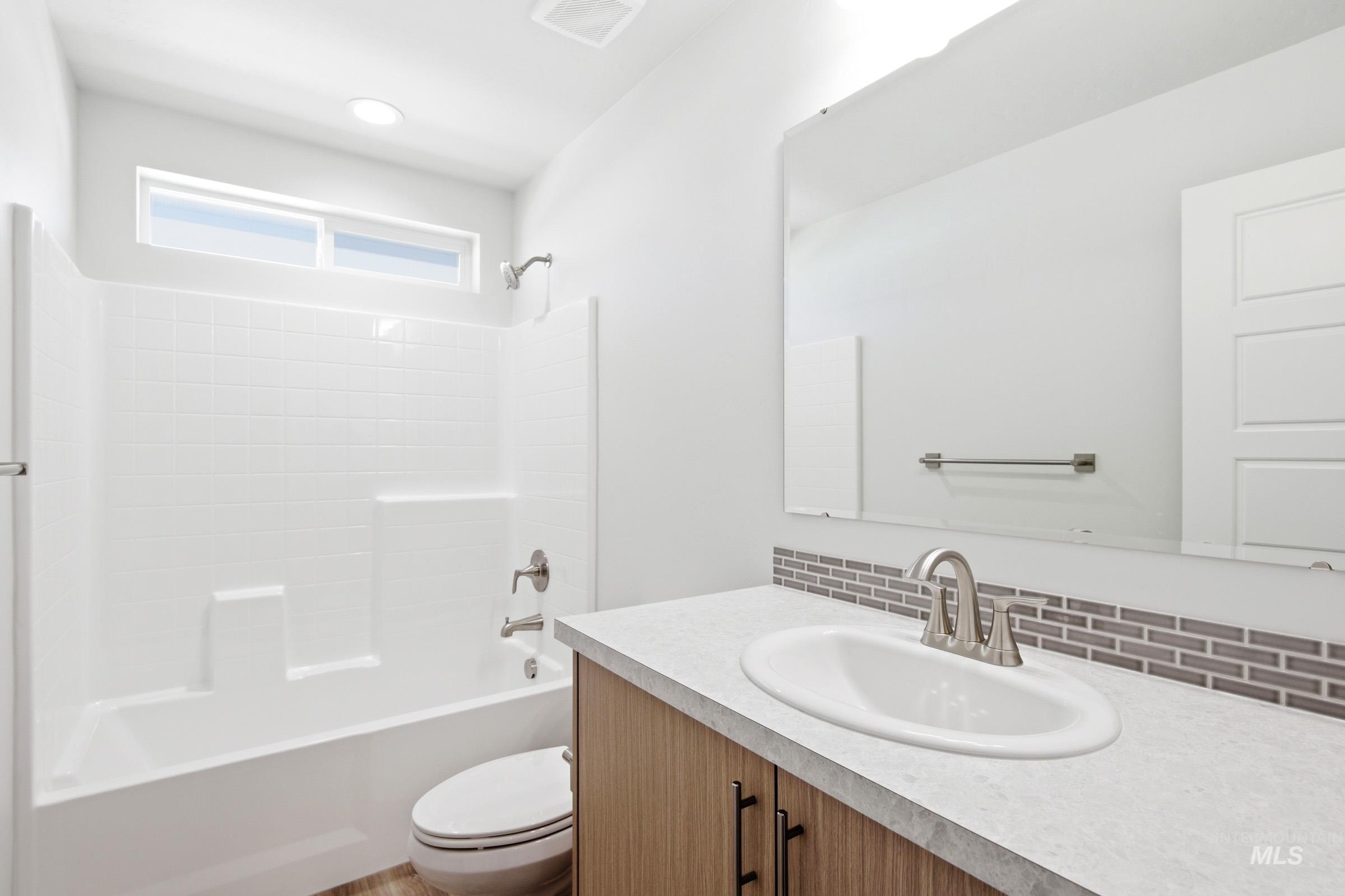12817 Decatur Street Nampa, ID 83651 - Photo 13 of 19 Contemporary bathroom featuring a white tub/shower combination with subway tile surround, an oval undermount sink, a light wood-finish vanity with dark hardware, a full-width mirror, and a transom window