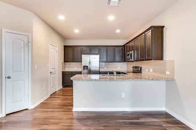 a kitchen with stainless steel appliances granite countertop a refrigerator a stove top oven a sink and dishwasher with wooden floor