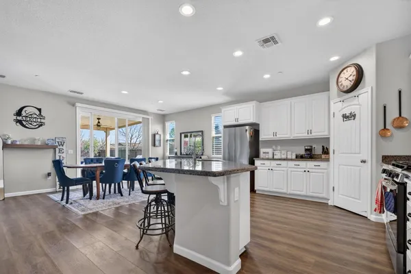 a kitchen with stainless steel appliances granite countertop a stove top oven a sink a dining table and chairs with wooden floor