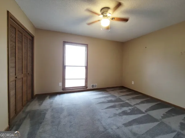 an empty room with chandelier fan and windows