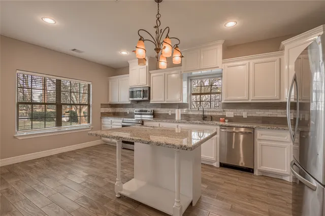 a kitchen with stainless steel appliances granite countertop a stove a sink dishwasher a refrigerator and white cabinets with wooden floor