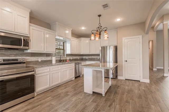 a kitchen with white cabinets stainless steel appliances and wooden floor