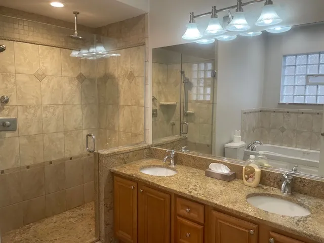 a bathroom with a granite countertop double vanity sink a shower and a mirror