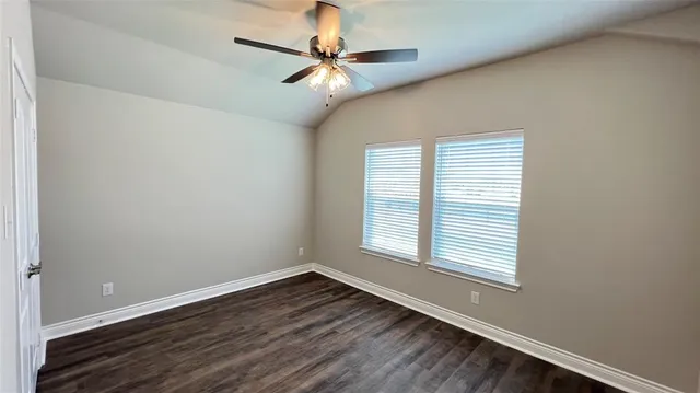 an empty room with wooden floor fan and windows