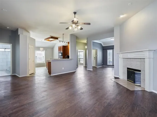 an empty room with wooden floor fireplace chandelier and a kitchen