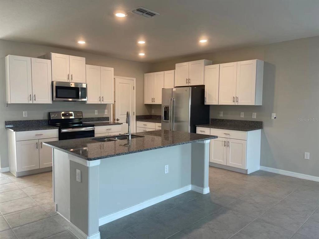 31875 Sun Kettle Loop Wesley Chapel, FL 33545 - Photo 6 of 23 a kitchen with stainless steel appliances granite countertop a refrigerator stove a sink a microwave and cabinets