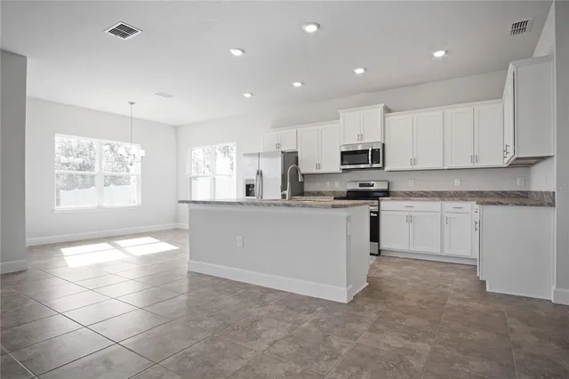 a kitchen with stainless steel appliances granite countertop a stove top oven a sink a refrigerator and white cabinets