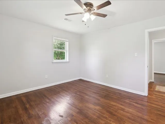 an empty room with wooden floor fan and windows