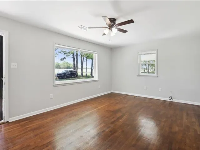 a view of an empty room with wooden floor and a window
