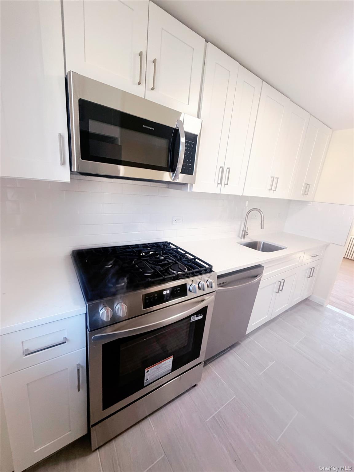 64-11 Springfield Boulevard, Unit B Queens, NY 11364 - Photo 8 of 11 a kitchen with stainless steel appliances a stove a microwave and white cabinets