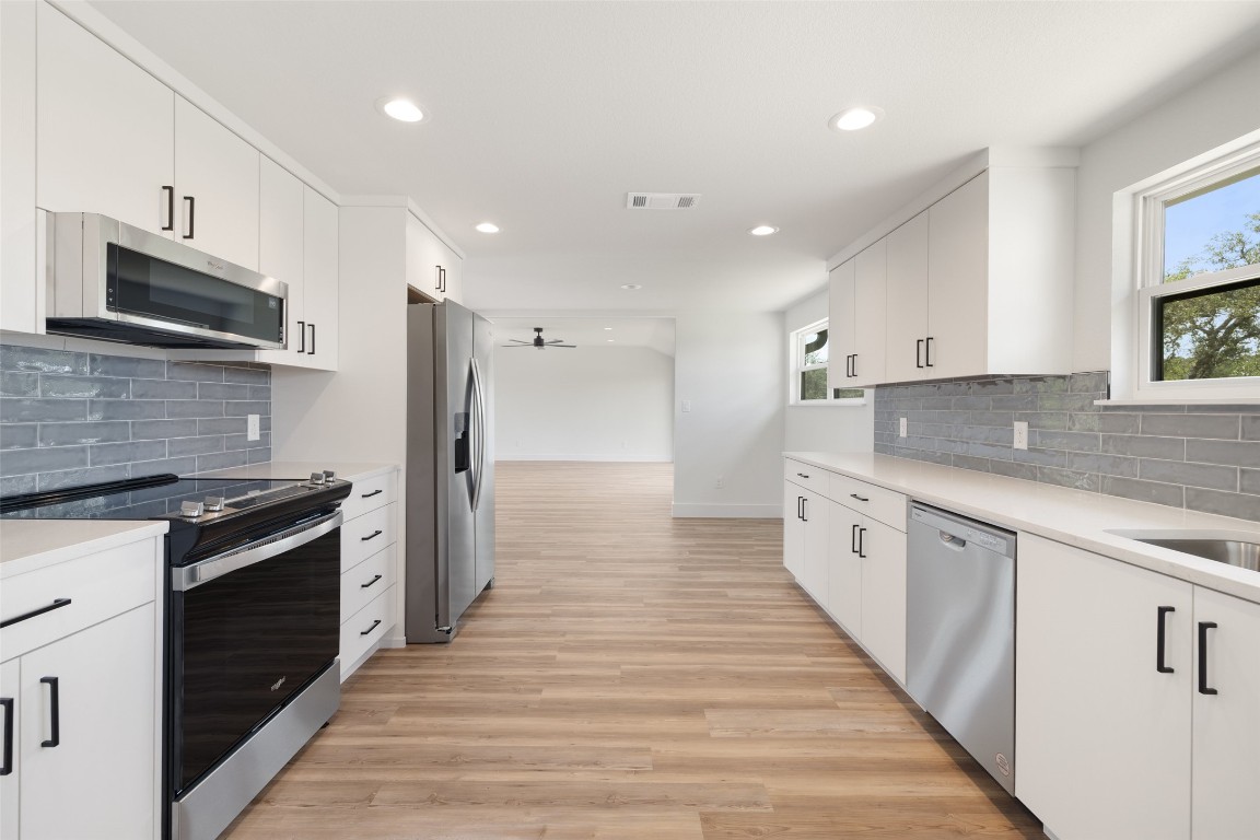 11151 Highway 71 Spicewood, TX 78669 - Photo 10 of 40 Unit A galley-style kitchen featuring stainless steel appliances, tasteful backsplash, light wood-style LPV flooring, white cabinets, and recessed lighting.