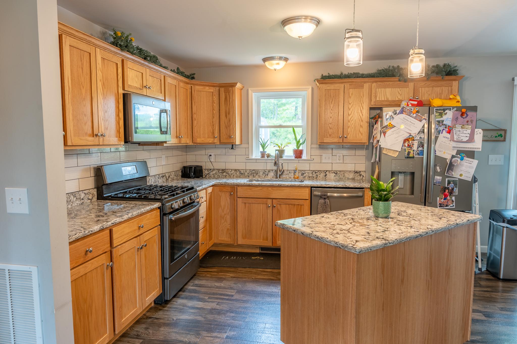 56 Ahrens Road Parksville, NY 12768 - Photo 5 of 23 Kitchen with appliances with stainless steel finishes, dark wood-type flooring, decorative backsplash, a center island, and light stone counters