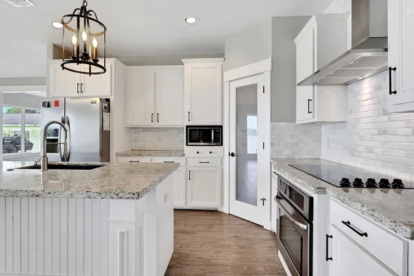 a kitchen with stainless steel appliances granite countertop a refrigerator a sink dishwasher a oven and white cabinets with wooden floor