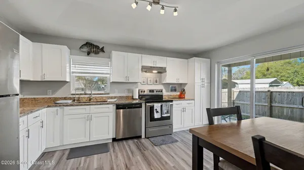 a kitchen with stainless steel appliances granite countertop a stove a sink dishwasher a refrigerator white cabinets and wooden floor