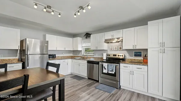 a kitchen with kitchen island granite countertop a stove a sink dishwasher a refrigerator and white cabinets with wooden floor