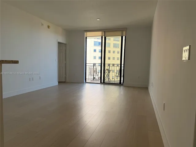 an empty room with wooden floor and windows with curtains