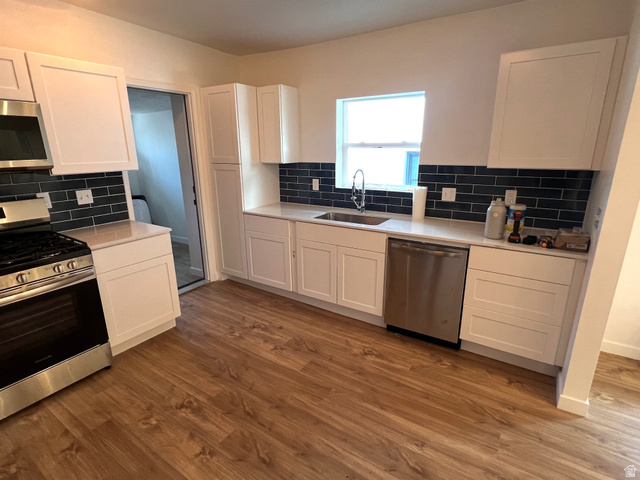 545 23rd Street Ogden, UT 84401 - Photo 6 of 28 Kitchen featuring wood-finish flooring, white cabinetry, dark subway tile backsplash, white countertops, and stainless steel appliances