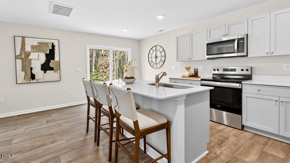 6037 Sodium Street Raleigh, NC 27610 - Photo 8 of 27 a kitchen with stainless steel appliances granite countertop a stove a sink a microwave a dining table and chairs with wooden floor