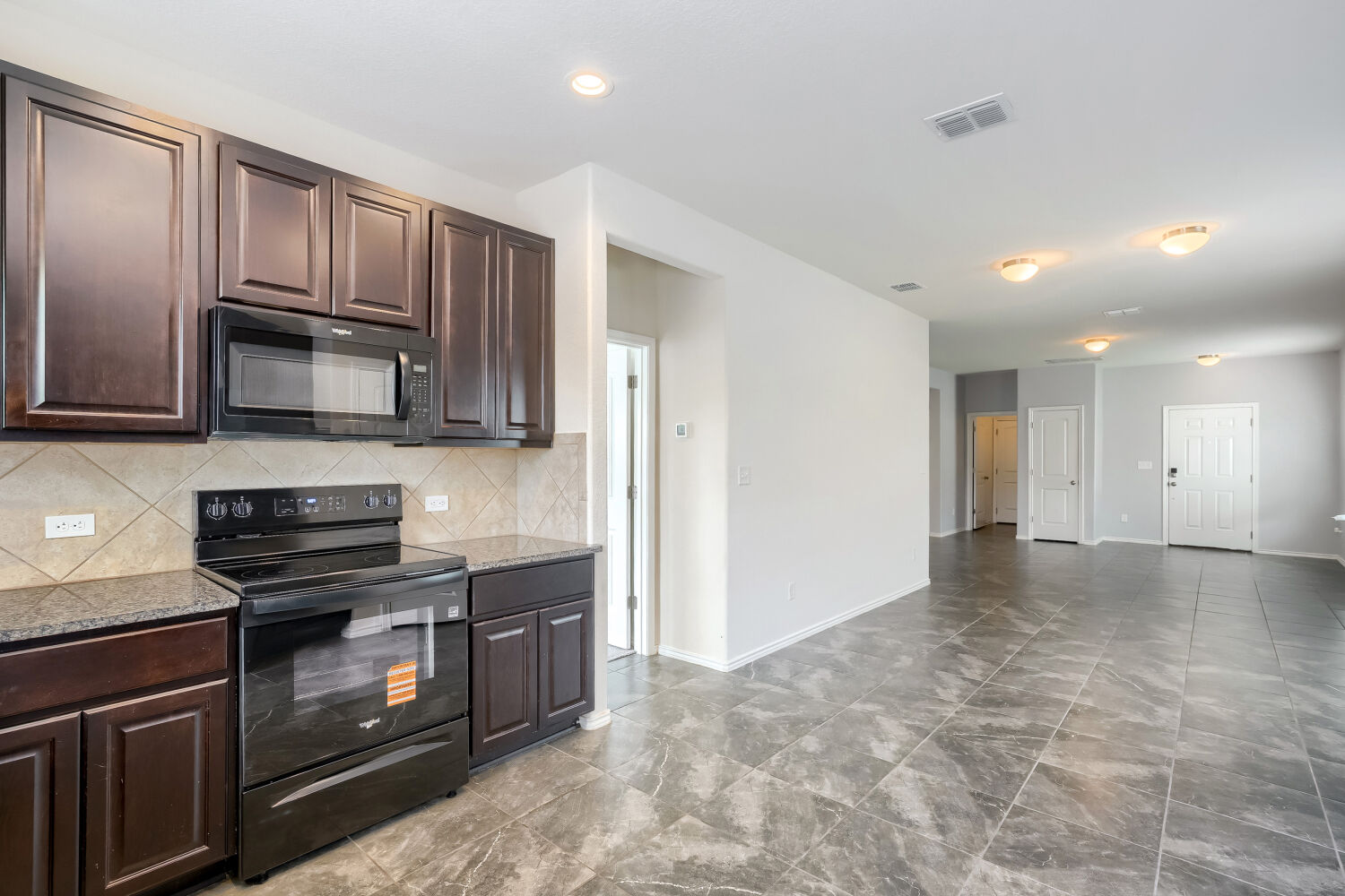 2420 Ranger Pass Seguin, TX 78155 - Photo 10 of 28 Kitchen area featuring dark wood-finish cabinetry, black appliances, a stone-finish countertop, and a tiled backsplash