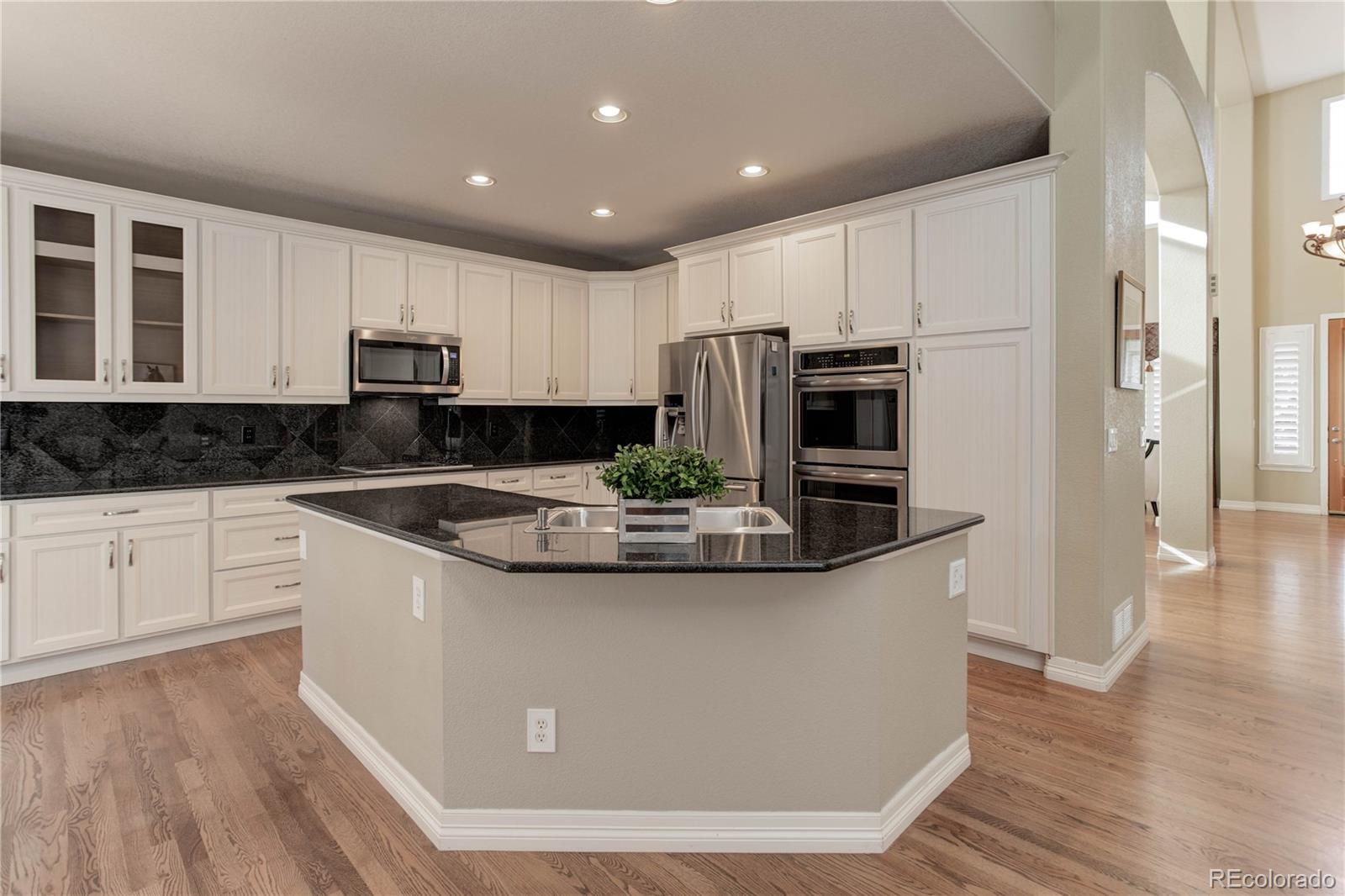 2720 Rockbridge Way Highlands Ranch, CO 80129 - Photo 12 of 39 a kitchen with stainless steel appliances granite countertop a stove a refrigerator a sink and white cabinets with wooden floor