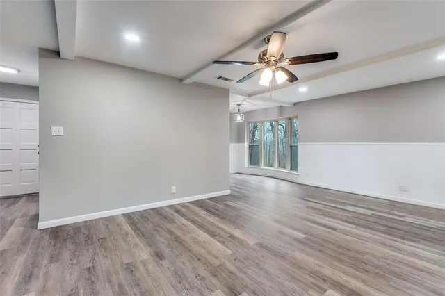 an empty room with wooden floor chandelier fan and windows