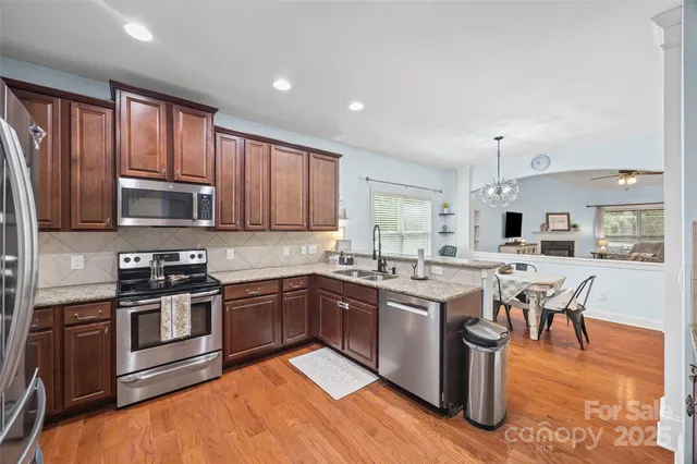 a kitchen with stainless steel appliances granite countertop a stove top oven a sink dishwasher a dining table and chairs with wooden floor