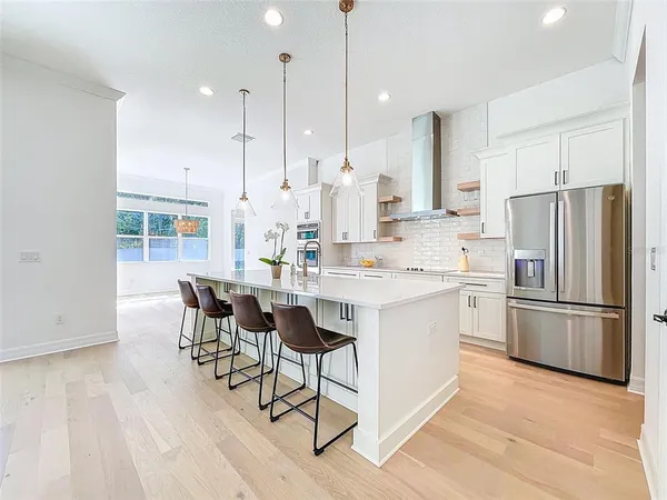 a kitchen with stainless steel appliances kitchen island granite countertop a refrigerator a stove a sink and white cabinets with wooden floor